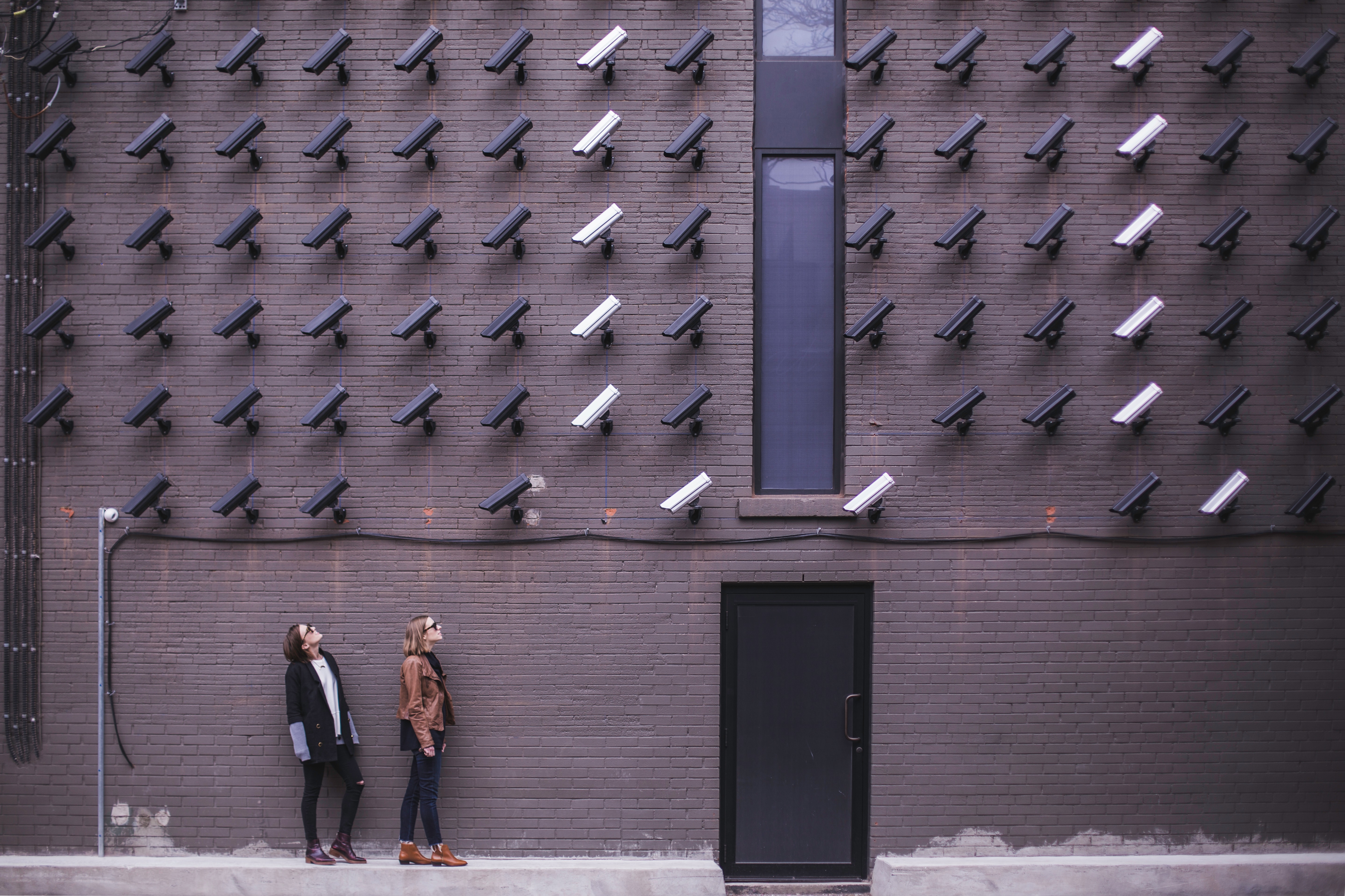 Two women looking up at a wall covered in security cameras