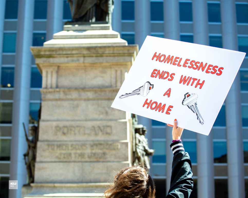 Person holding sign reading "homelessness ends with a home"