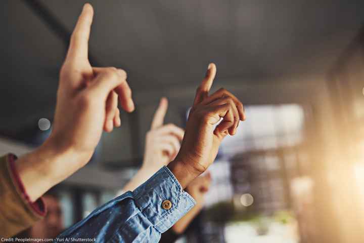 Several hands raising, one of which belongs to a Black person.