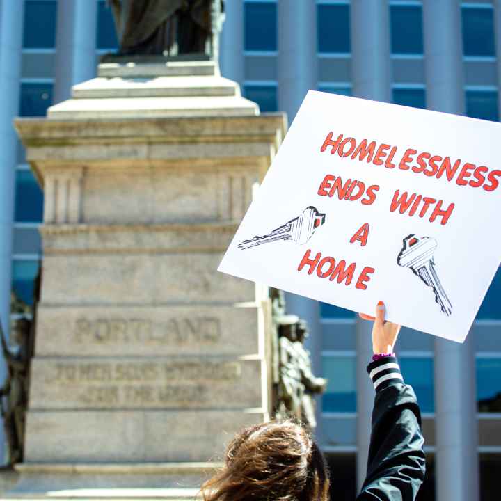 Person holding sign reading "homelessness ends with a home"