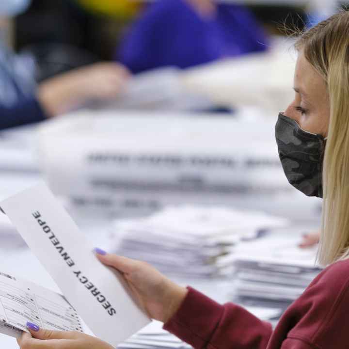 A woman with a surgical mask opening absentee ballots.